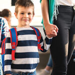 Young Caucasian boy with backpack holding a woman's hand while riding a bus