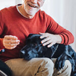 White male senior sitting in wheelchair, cuddling black dog that has his head in the man's lap