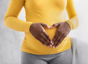 Close up of pregnant BIPOC woman's hands making a heart shape over her belly